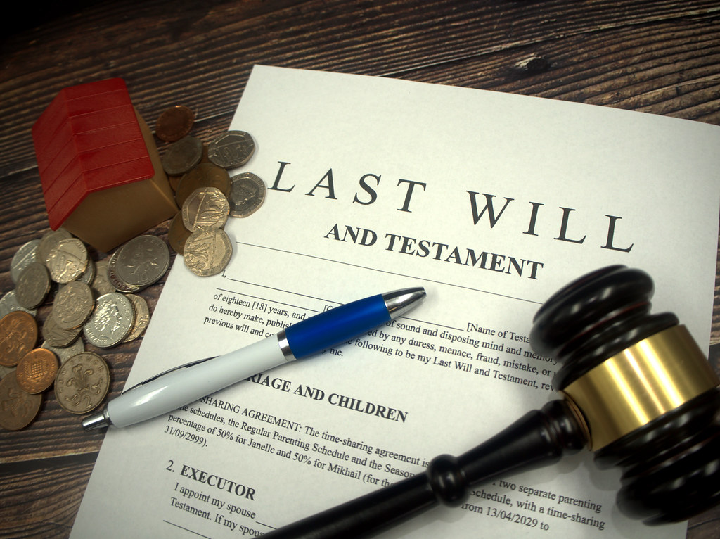 A last will and testament document beside a gavel, a model house and cash, representing crypto inheritance and estate planning