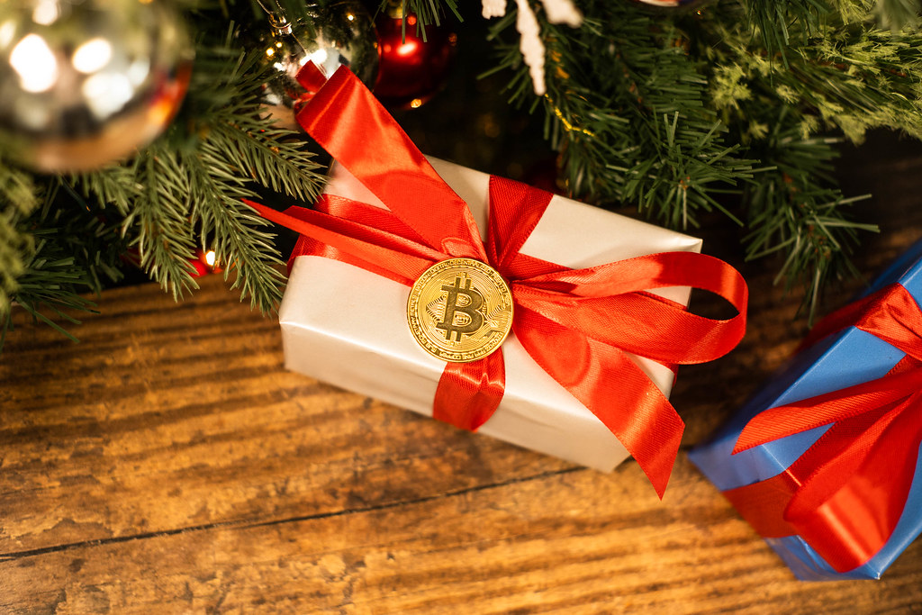 A wrapped gift box beside a physical Bitcoin coin, illustrating giving cryptocurrency as a present